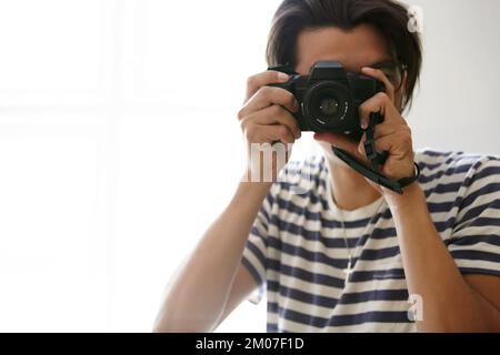 Sorridi. Vista ritagliata di un giovane ragazzo che sorregge una macchina fotografica per scattare una foto. Foto Stock