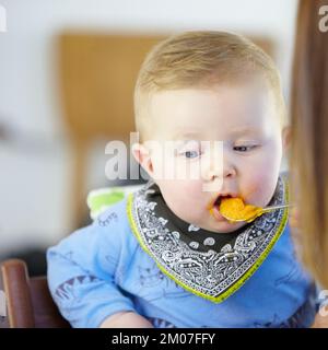 Provare cose nuove - nutrizione infantile. Il giovane bambino che viene nutrito nel suo seggiolone. Foto Stock