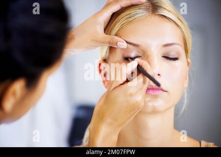 Questo lavoro richiede una mano costante. Bella giovane donna che ha il suo trucco applicato da uno stilista. Foto Stock