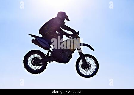 Sospeso nello spazio. Silhouette di un motociclista che salta contro un cielo blu. Foto Stock