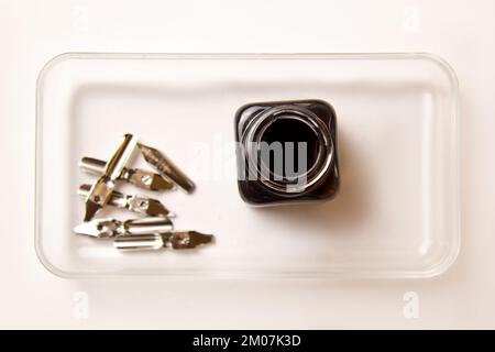 flacone di inchiostro con punte metalliche per penna su sfondo bianco. cancelleria sulla scrivania bianca, vista dall'alto. lezioni di ortografia ed esercizi di caligrafia. T Foto Stock