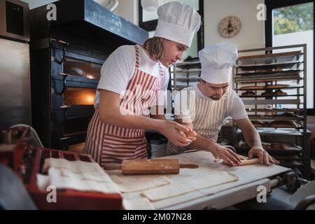 Uomo con giù sindromi aiutare a preabbinare il pane in panetteria con il suo collega. Concetto di integrazione delle persone con disabilità nella società. Foto Stock