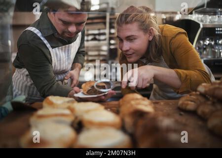 Uomo con sindrome di Down aiutare il suo collega in un caffè, tenendo dolci freschi. Concetto di integrazione delle persone con disabilità nella società. Foto Stock