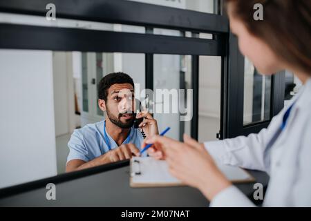 Giovane medico che parla alla reception dell'ospedale con la sua collega. Foto Stock