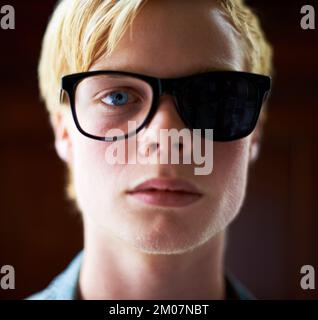 HES ha una visione parziale delle cose. Giovane ragazzo attraente che indossa occhiali da hipster con un lato oscurato fuori. Foto Stock