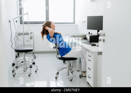 Giovane donna medico stretching alla scrivania dell'ufficio dell'ospedale. Foto Stock