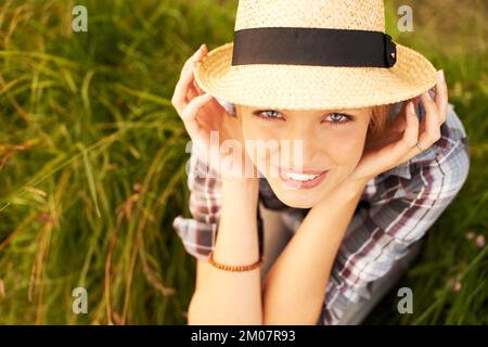 Youre mai completamente vestito senza un sorriso. Bella giovane donna in un campo mentre indossa una fedora di paglia. Foto Stock