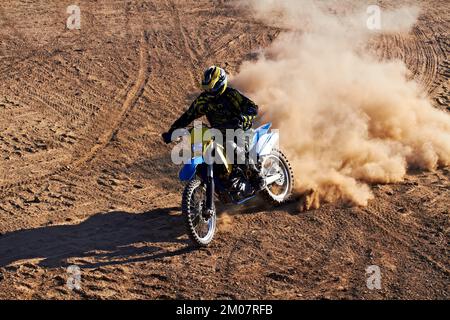 Lasciando i suoi concorrenti nella polvere. Un biker sterrato che corre lungo una pista con una nuvola di polvere che lo segue. Foto Stock