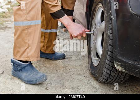 Uomo meccanico con cacciavite elettrico che sostituisce il pneumatico all'esterno. Servizio auto. Sostituire gli pneumatici sulle ruote con le mani. Concetto di installazione degli pneumatici Foto Stock