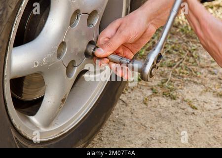 Processo di assistenza. Un uomo tiene uno pneumatico in garage. Sostituzione degli pneumatici invernali ed estivi. Concetto di sostituzione stagionale degli pneumatici Foto Stock