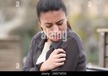 Donna stressata graffiare il braccio itchy in un parco Foto Stock