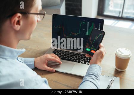 Vista rara immagine in primo piano ritagliata di un'applicazione intelligente di successo per il controllo del mercato valutario del crypto trader su smartphone e laptop, guardando le tabelle, pronta a investire, acquistare o vendere gettoni bitcoin Foto Stock