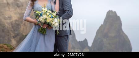 una coppia in piedi in un abbraccio con un bel bouquet di fiori, una ragazza vestita con un lungo vestito blu, un uomo vestito con un vestito. concetto di matrimonio Foto Stock