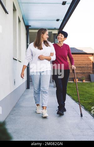 Ritratto verticale di un'infermiera e di una donna anziana che tiene la mano in mano, infermiera che dà sostegno alla donna anziana mentre cammina Foto Stock