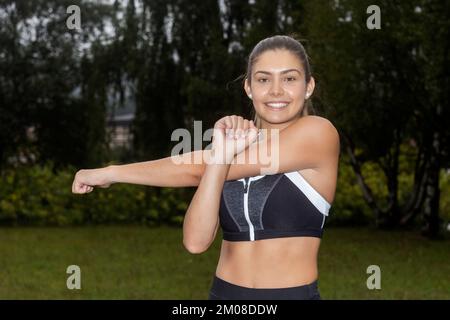 Forte donna sana e determinata che si allunga, allunga le braccia, si riscalda per l'esercizio fisico. La silhouette del giovane atleta prepara il corpo Foto Stock