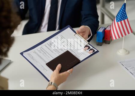 Primo piano di una donna che consegna il modulo di richiesta del visto al lavoratore dell'ufficio immigrazione degli Stati Uniti Foto Stock