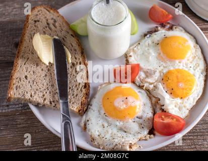 Piatto per la colazione con pane di segale, burro, yogurt alla mela fatto in casa e uova fritte, lato soleggiato su un tavolo di legno. Primo piano e vista dall'alto Foto Stock