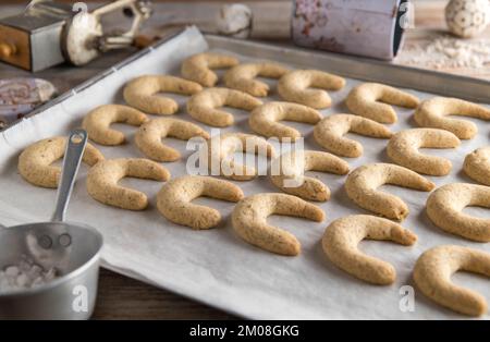 Biscotti di natale appena sfornati, vanillekipferl o cressents alla vaniglia su una teglia da forno con utensili da cucina vecchio stile. Foto Stock