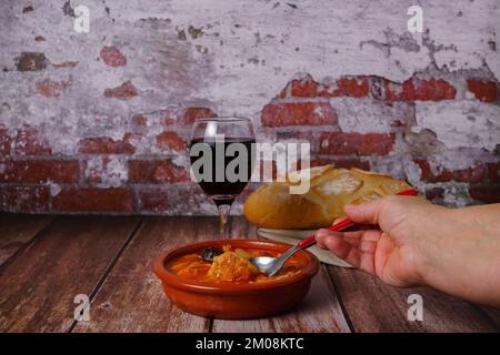 Casseruola di argilla con trippa in umido stile Madrid, piatti tipici spagnoli su un tavolo di legno con un muro di mattoni sullo sfondo. Foto Stock