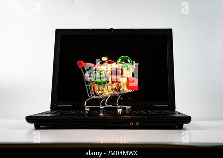 Carrello con palle di natale e ghirlande sulla tastiera del computer portatile. Sfondo semplice. Foto Stock