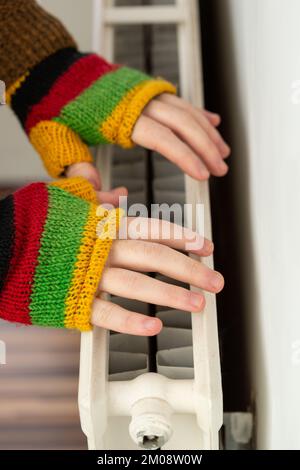 Primo piano delle mani nei guanti senza dita che si riscaldano contro un radiatore a gas Foto Stock