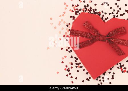 Scatola regalo rossa a forma di cuore legata con nastro scintillante.  Composizione festosa con confetti sparsi su sfondo beige Foto stock - Alamy