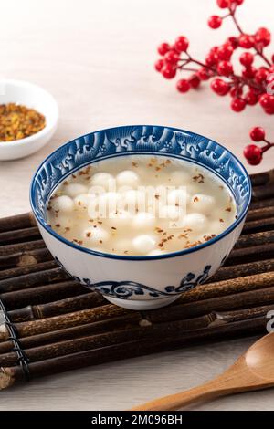 Piccolo tangyuan bianco (tang yuan, palle di gnocchi di riso glutinoso) con miele di osmanthus dolce e zuppa di sciroppo in una ciotola su fondo di tavolo di legno. Foto Stock