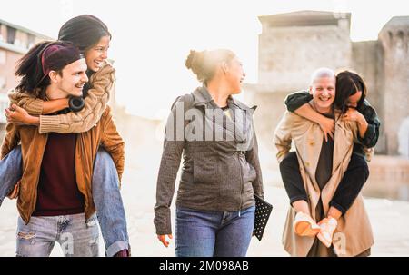 Giovani genuini che camminano insieme sul movimento del piggyback - concetto di stile di vita con gli amici felici che hanno divertimento genuino intorno alle strade della città Foto Stock
