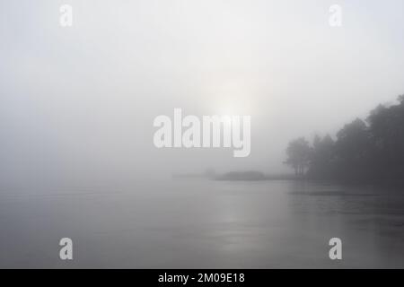 Una piccola casa sulla costa della svezia e sole che si infrange attraverso la fitta nebbia in inverno Foto Stock