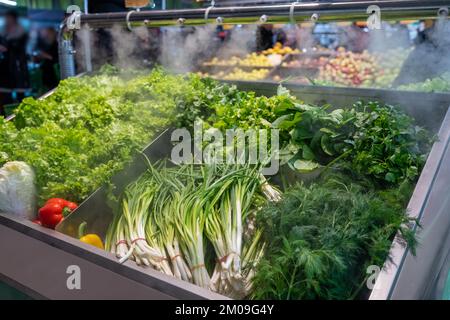 Vendita di verdure fresche verdi - insalata di lattuga, prezzemolo, aneto, cipolle verdi, erbe aromatiche. Erbe fresche in esposizione presso il negozio di alimentari sotto il vapore di acqua di raffreddamento. Foto Stock