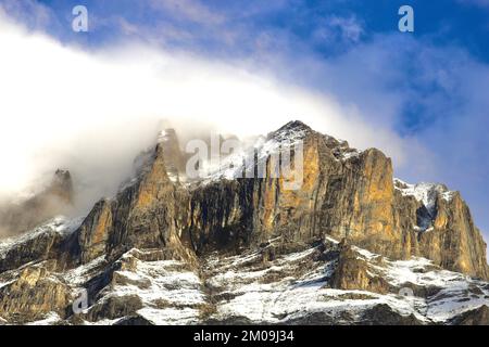 Un'immagine panoramica di montagne rocciose brune e nere ricoperte di neve e nuvole bianche Foto Stock