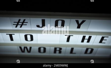 Scatola luminosa con la frase "# Joy to the World" illuminata su di essa posta in ombra e sfondo scuro Foto Stock