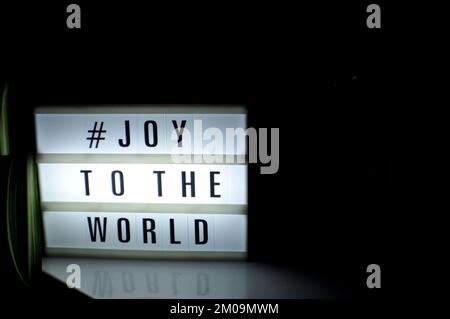 Scatola luminosa con la frase "# Joy to the World" illuminata su di essa posta in ombra e sfondo scuro Foto Stock