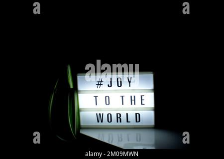 Scatola luminosa con la frase "# Joy to the World" illuminata su di essa posta in ombra e sfondo scuro Foto Stock