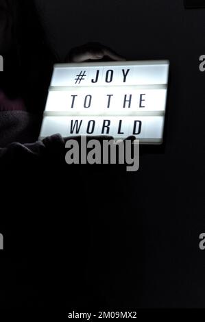 La scatola luminosa è tenuta con la frase "# Joy to the World" illuminata su di essa posta in ombra e su sfondo scuro Foto Stock