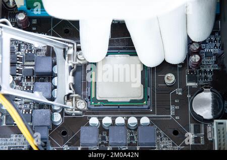 Vista dall'alto della scheda madre e del tecnico sull'inserimento del chip della CPU. Foto Stock