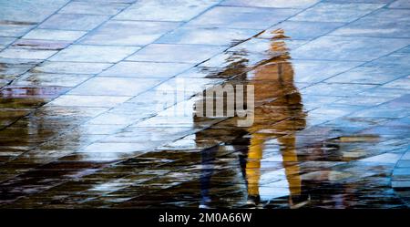 Astratto blurry silhouette ombra riflessi di persone irriconoscibili riflessioni a piedi sul bagnato strada della città strada marciapiede in un giorno di primavera piovoso Foto Stock