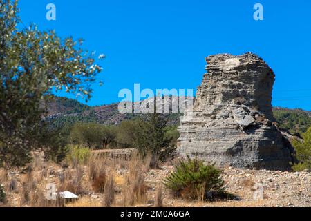 Ulivo e grande roccia in un tipico paesaggio greco. Clima arido e cielo azzurro soleggiato. Isola di Rodi, Grecia. Foto Stock