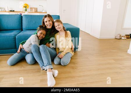 Bella madre sorridente con le sue due figlie felici seduti sul pavimento in un accogliente soggiorno a casa Foto Stock