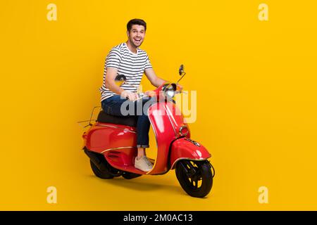 Foto a tutta lunghezza di bel ragazzo impressionato vestito a strisce t-shirt equitazione ciclomotore spazio vuoto isolato sfondo di colore giallo Foto Stock