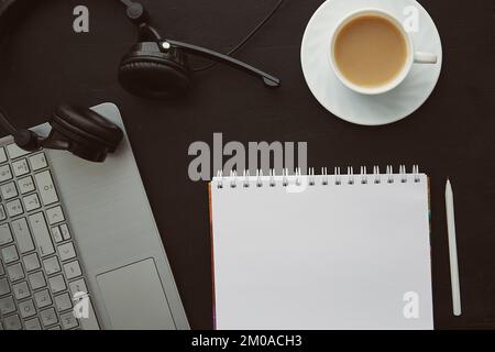 Elegante ufficio a posa piatta: Notebook, tazza di caffè, computer portatile e cuffie. Concetto di obiettivi e risoluzioni per il nuovo anno Foto Stock