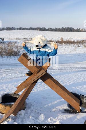 Un bambino irriconoscibile siede su una barriera anticarro di ferro fatta per bloccare l'offensiva militare russa in Ucraina. I bambini chiedono di fermare il Foto Stock