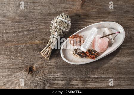 Vassoio porta incenso in ceramica bianca con pietre di cristallo minerale e bastone Aroma e un pacchetto di salvia Sage sullo sfondo rustico di legno Foto Stock