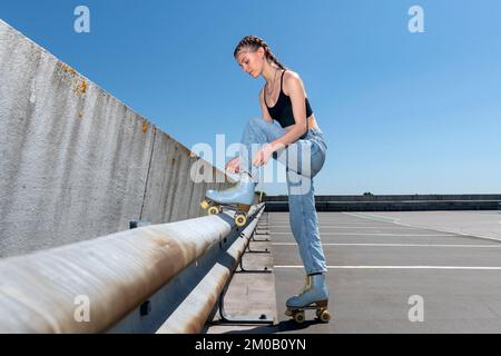 Ragazza che lega i suoi pattini del rullo, priorità bassa urbana. Preparazione per il pattinaggio su rotelle. Foto Stock