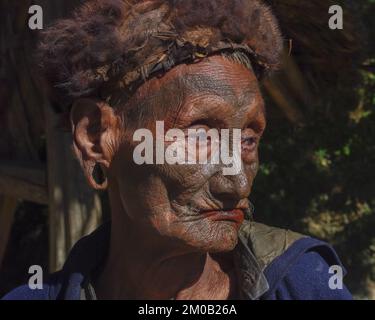 Mon District, Nagaland, India - 11 25 2013 : Ritratto della vecchia tribù Naga Konyak cacciatore capo guerriero con tatuaggio facciale tradizionale con cappello di pelliccia Foto Stock