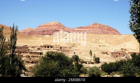 Villaggio tra Herat e Qala-e-Naw, provincia di Herat in Afghanistan con uno sfondo di colorate montagne rosse in una parte remota dell'Afghanistan occidentale. Foto Stock