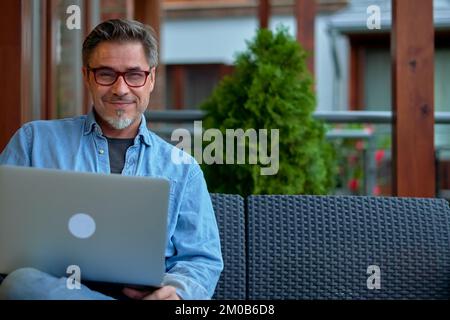 Ritratto all'aperto di un uomo medio adulto nel 50s, felice sorriso fiducioso. Lavorare con un computer portatile in ufficio. Età matura, mezza età, ribassista. Foto Stock