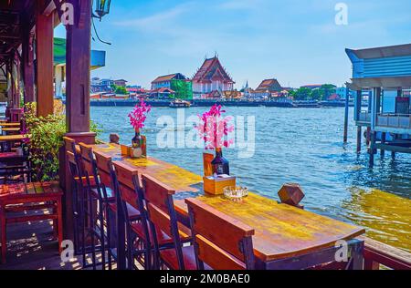 Il cafè all'aperto sul fiume con orchidee in bottiglia sui tavoli si affaccia sul Chao Phraya a Bangkok, Thailandia Foto Stock