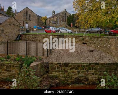 Con il fiume Seven in primo piano, alberi abbattuti, auto parcheggiate e la chiesa in Rosedale Abbey. North Yorkshire Foto Stock