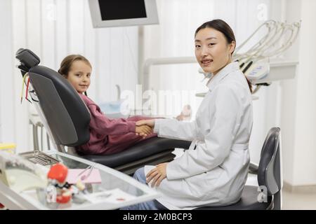 Giovane donna pediatrica dentista scuotendo cute poco sorridente bambina paziente mano dopo il trattamento dei denti, curando con successo in clinica dentale moderna e luminosa. Foto Stock